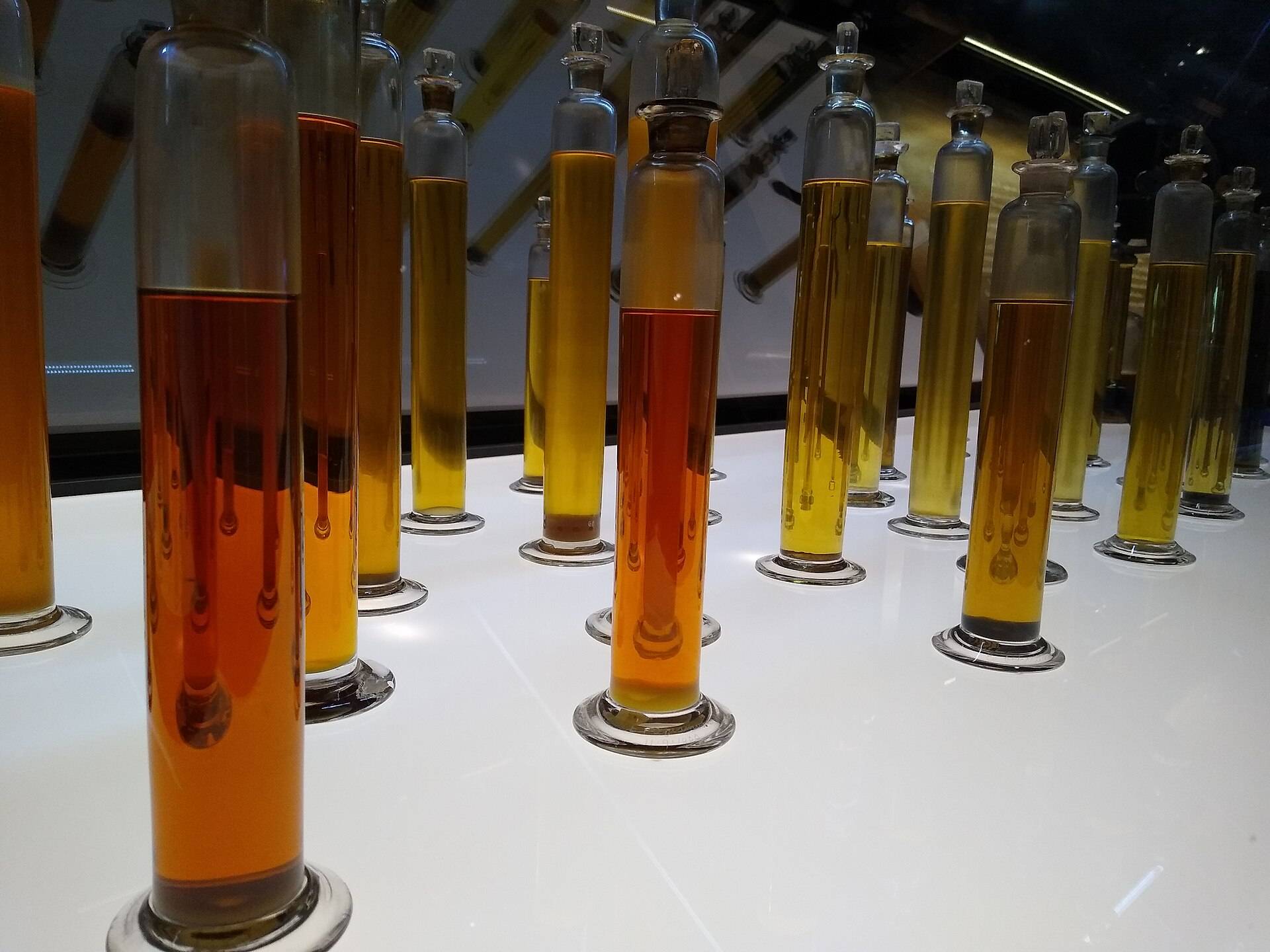Rows of tall glass cylinders holding amber and gold oils on a white bench