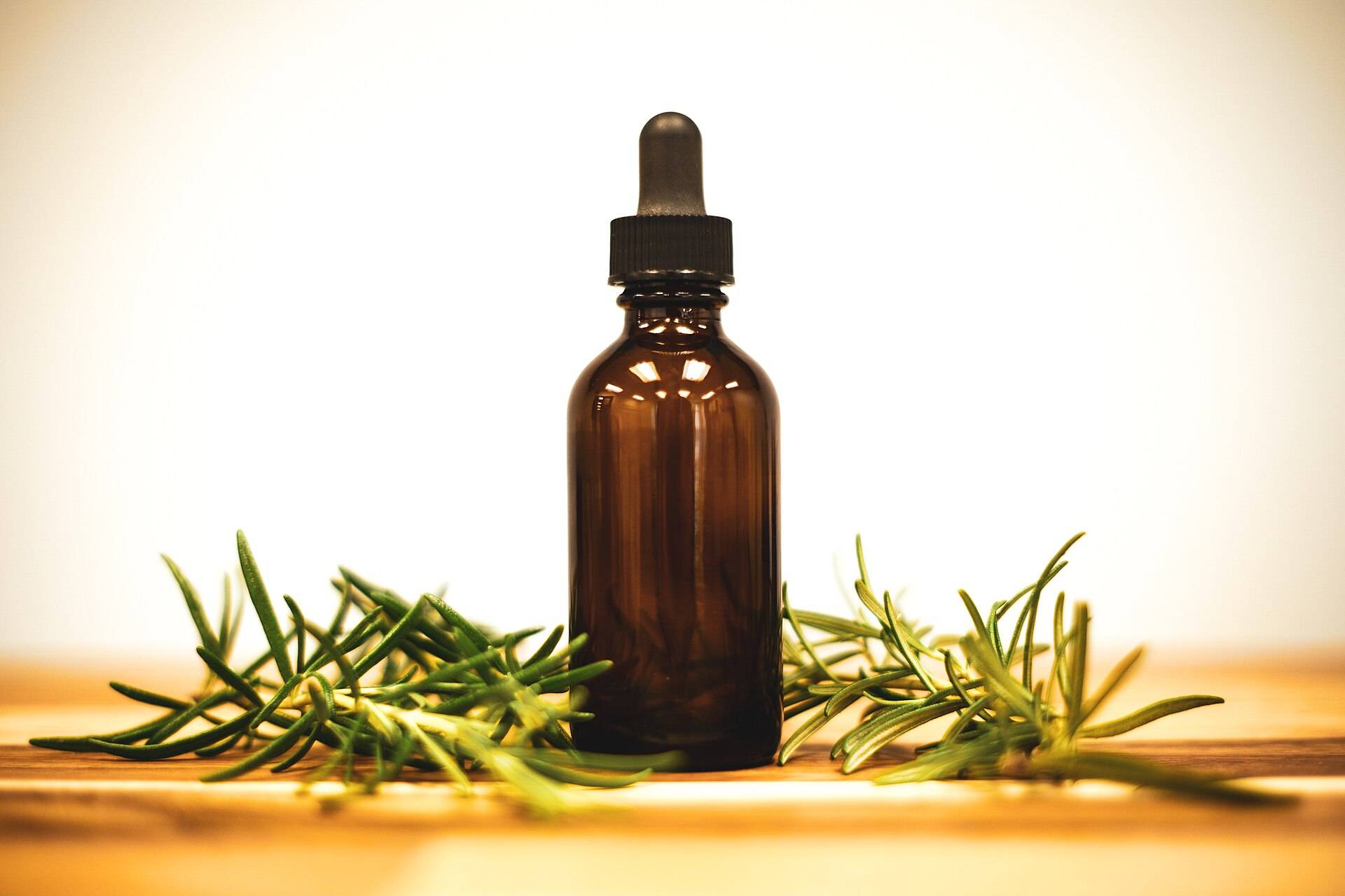 An unlabelled amber dropper bottle among rosemary sprigs on a wooden table