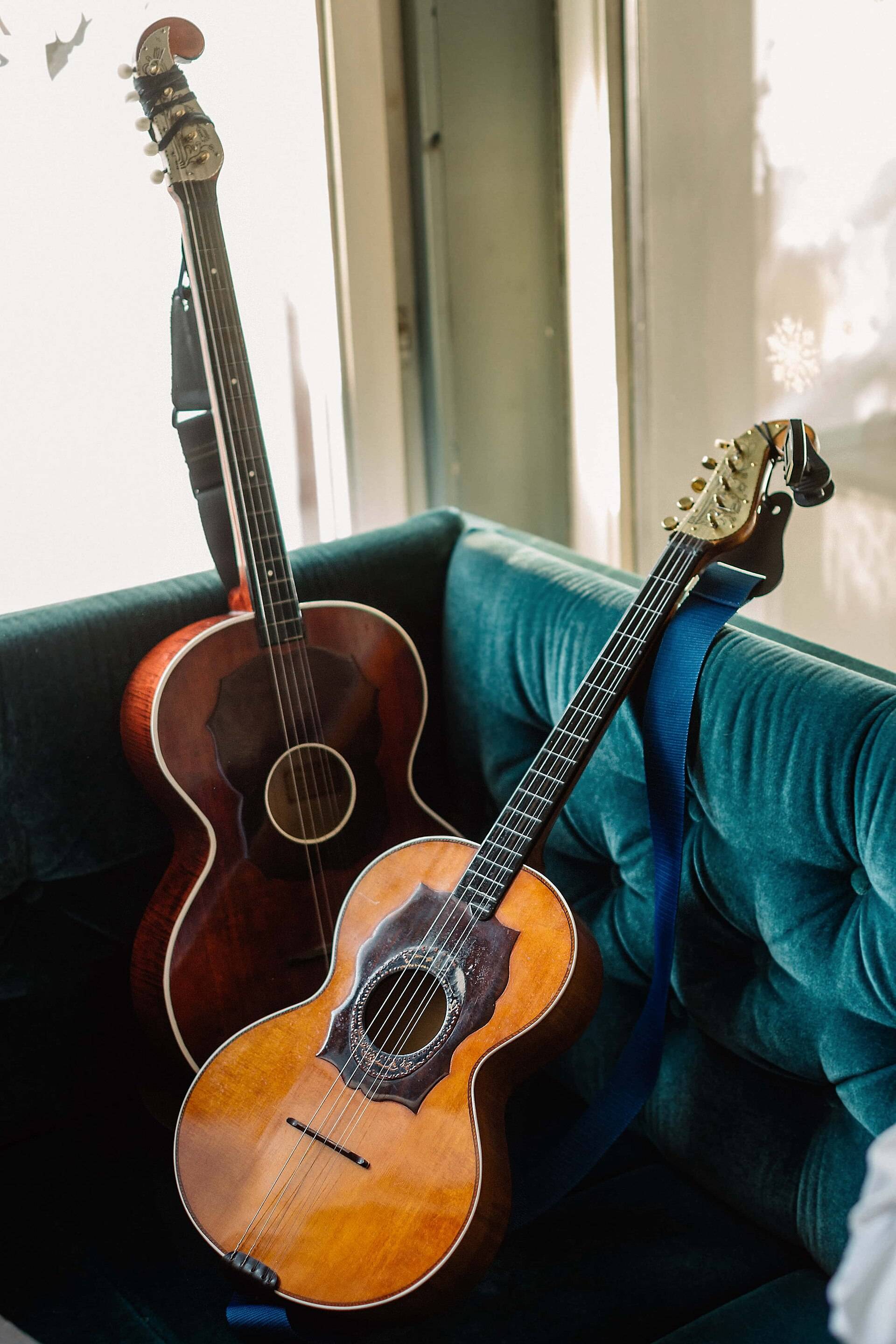 Two old acoustic guitars resting in a velvet armchair by a sunny window