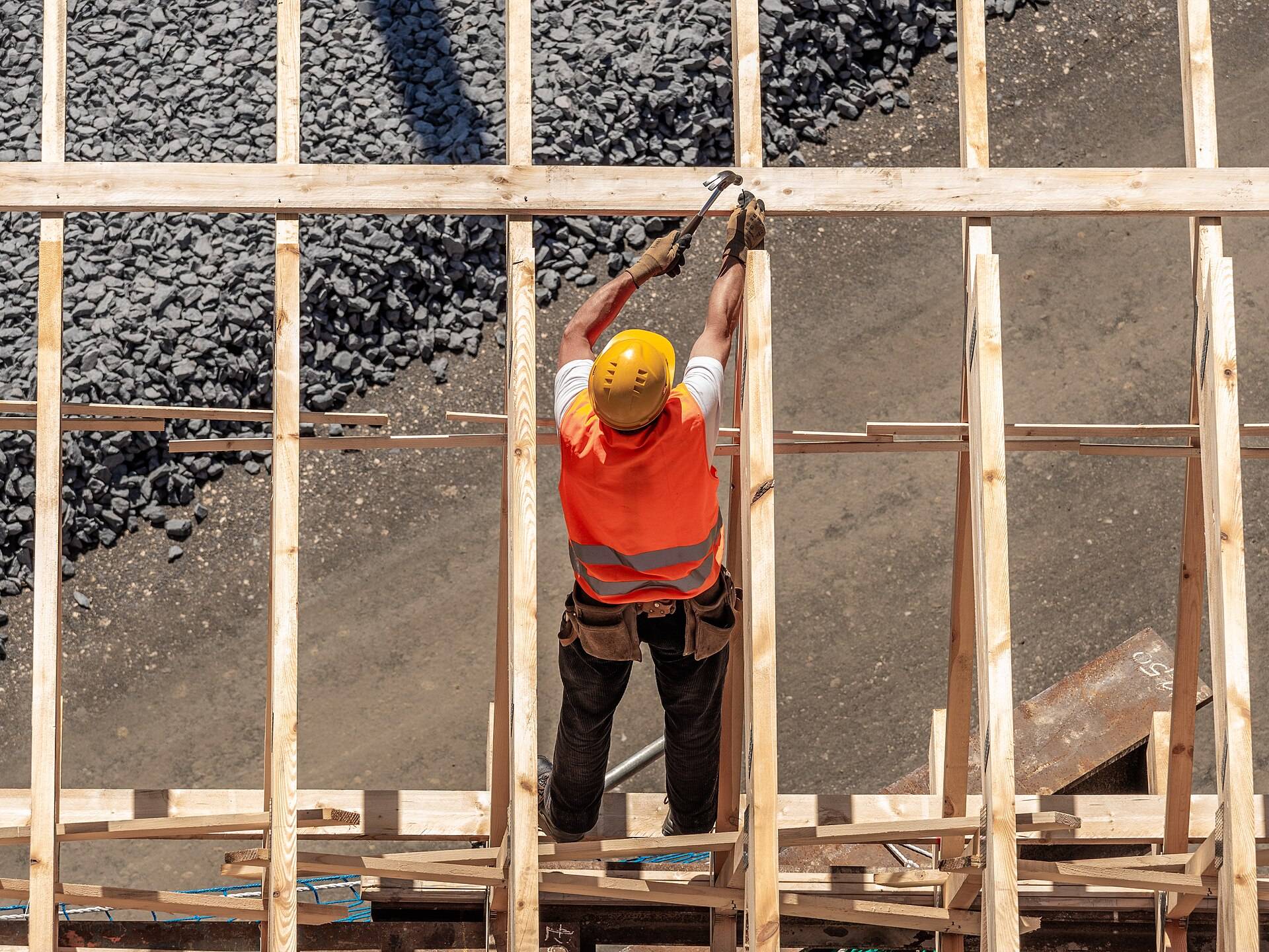 A carpenter in a hard hat nailing a timber frame, seen from above