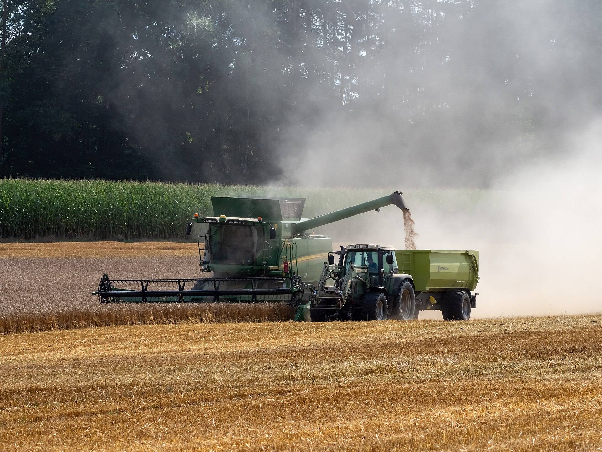 A combine harvester unloading grain into a tractor trailer, side-on in a cloud of dust
