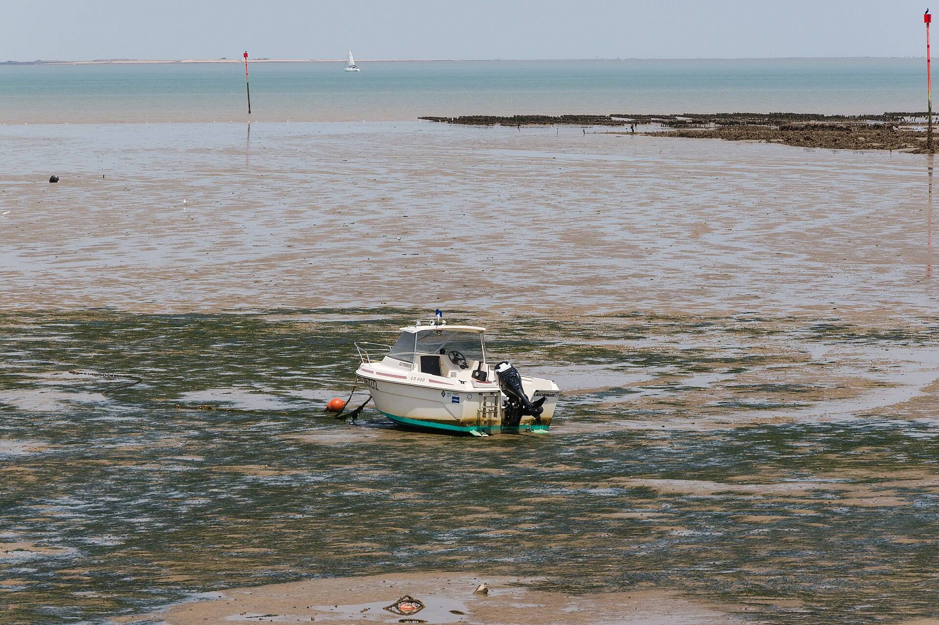 A small motorboat left on wet sand flats by the tide, marker posts far off