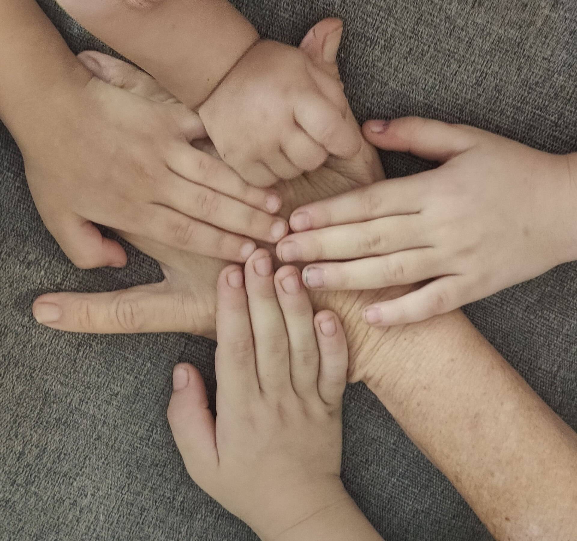 Small children's hands laid together on their grandmother's hand