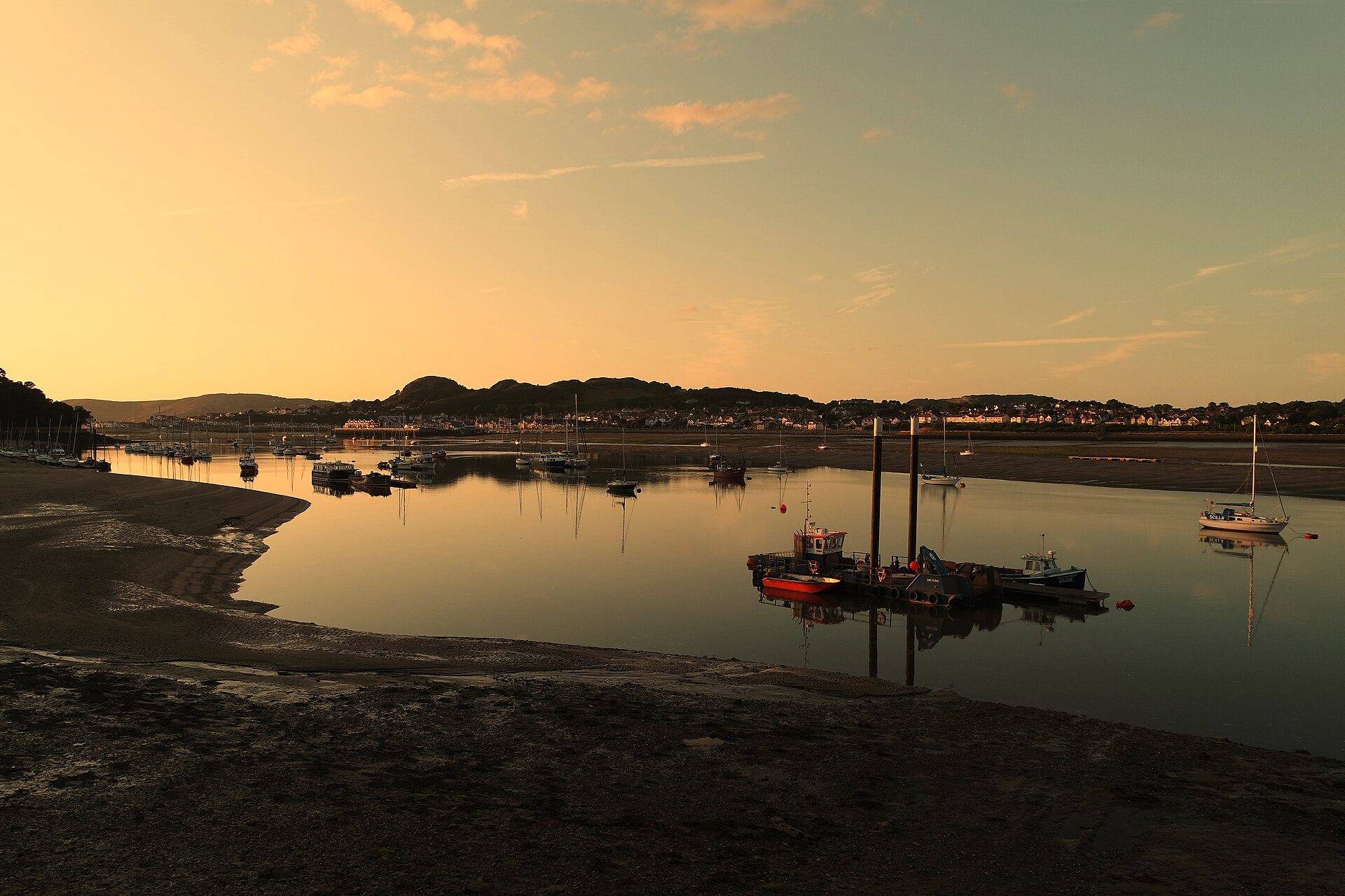A calm estuary at dusk, boats at their moorings under an amber sky