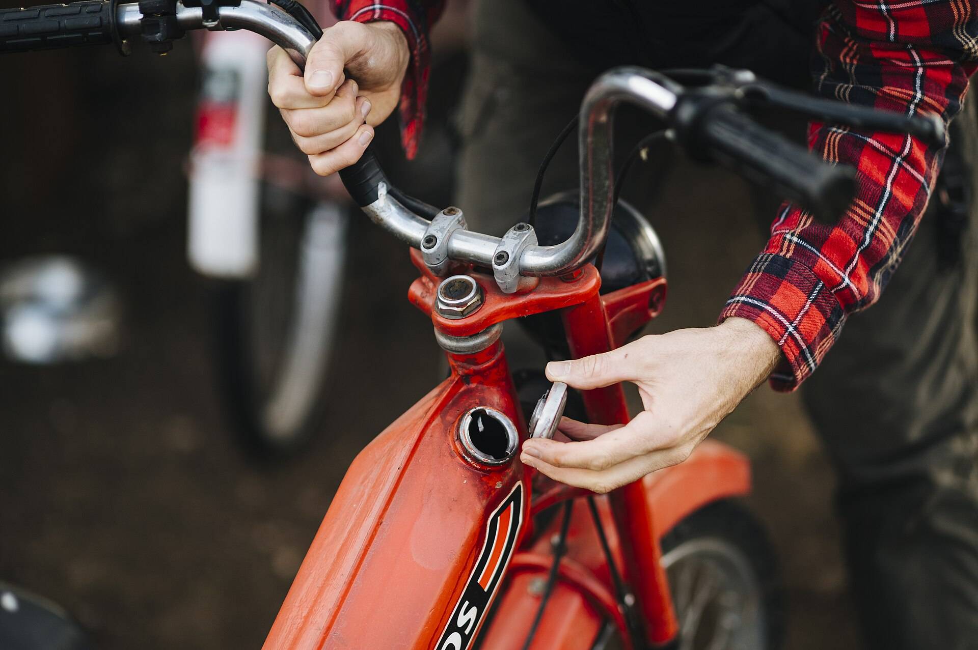 Hands opening the fuel cap of a red moped below its handlebars