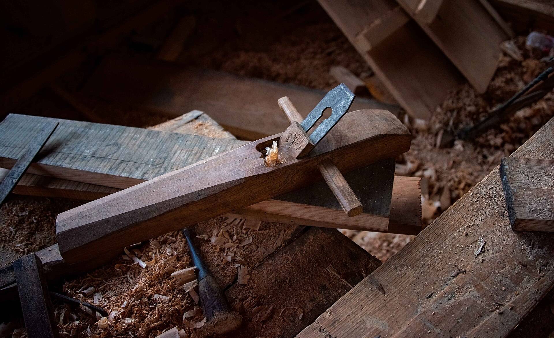 A worn wooden plane resting in curled shavings on an old workbench