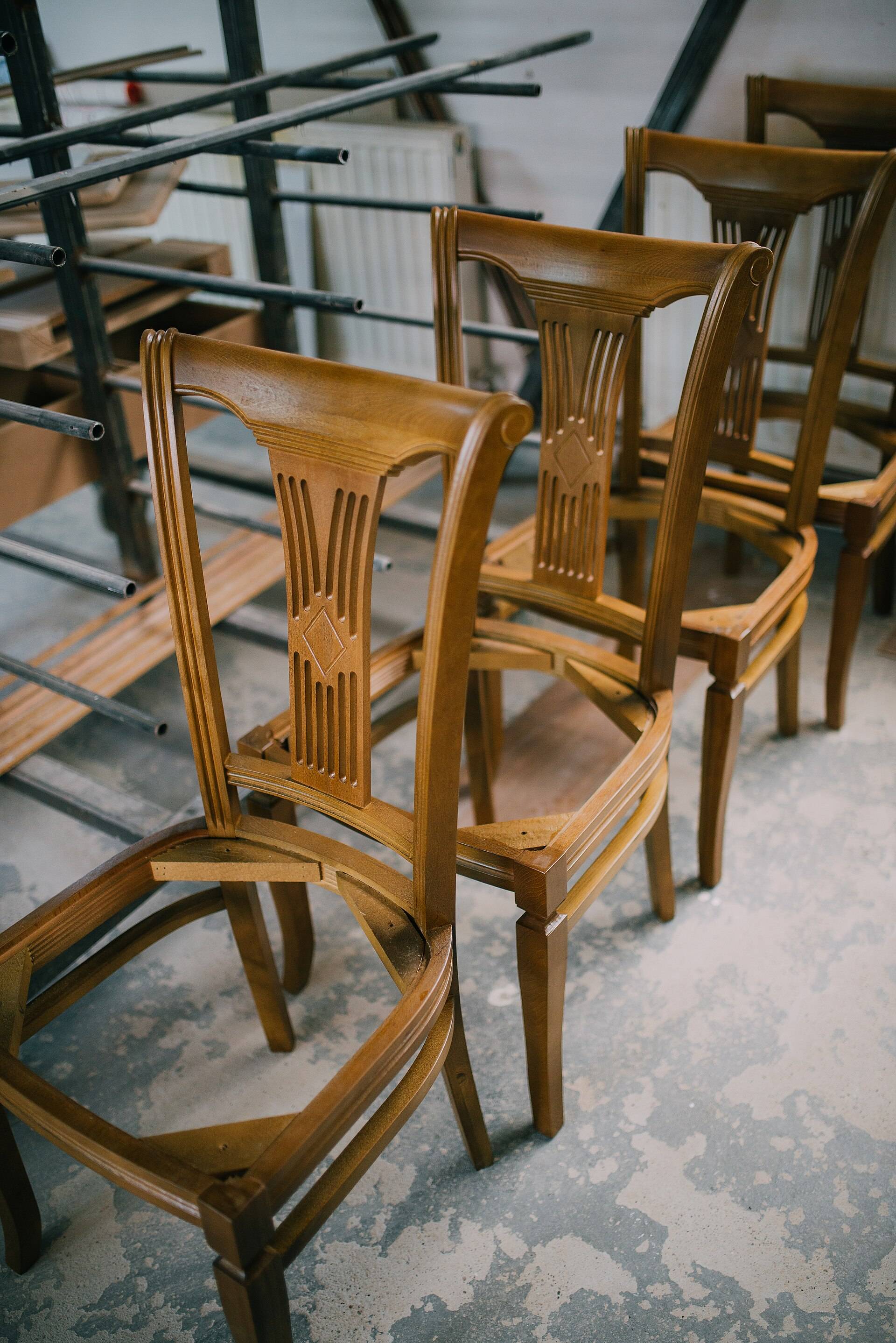Wooden chairs part way through restoration, stacked on benches in a furniture workshop