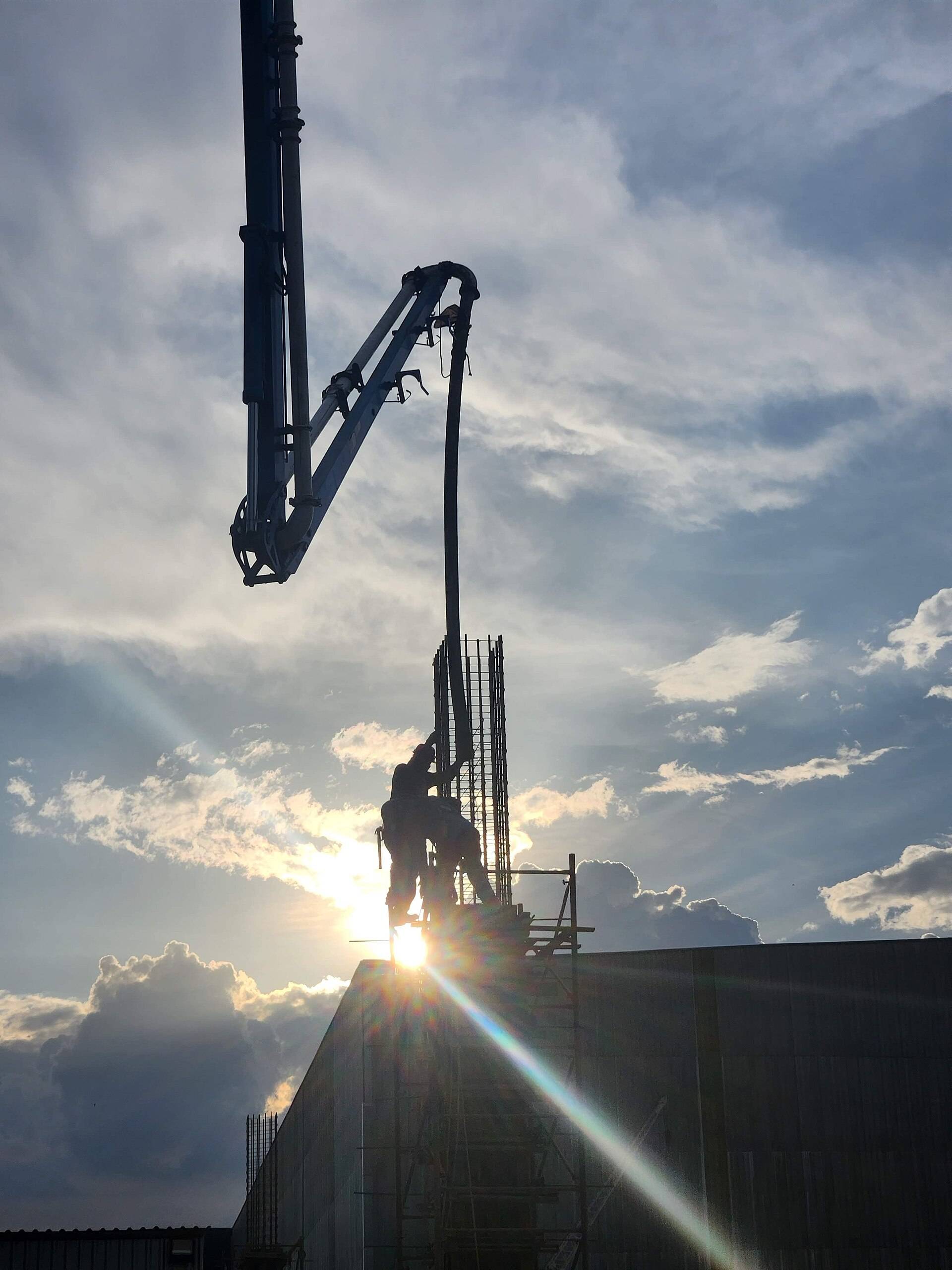 A pump boom feeding concrete into a column against a low sun