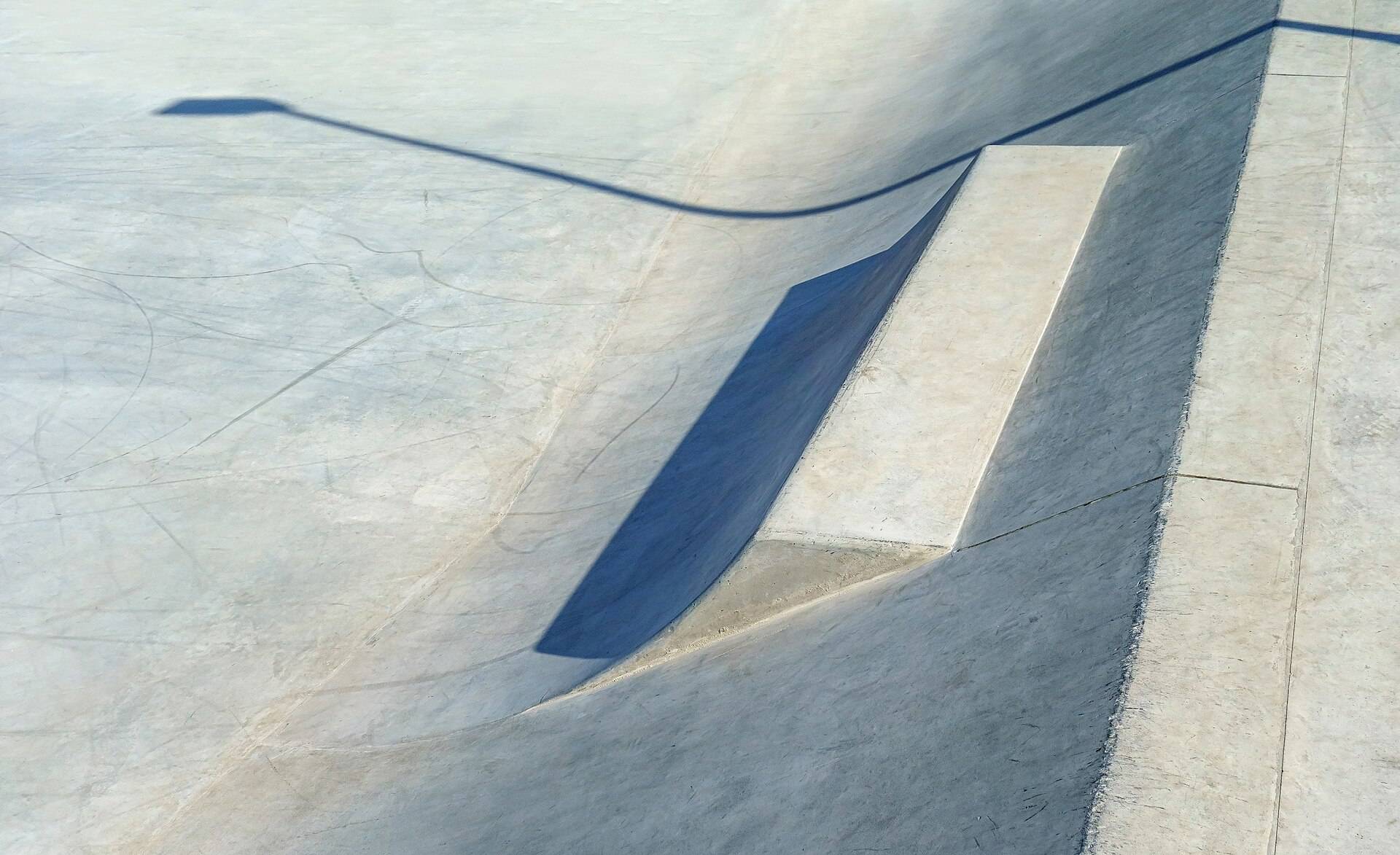 A smooth concrete skate ramp and its coping, a lamp post's shadow drawn across the deck