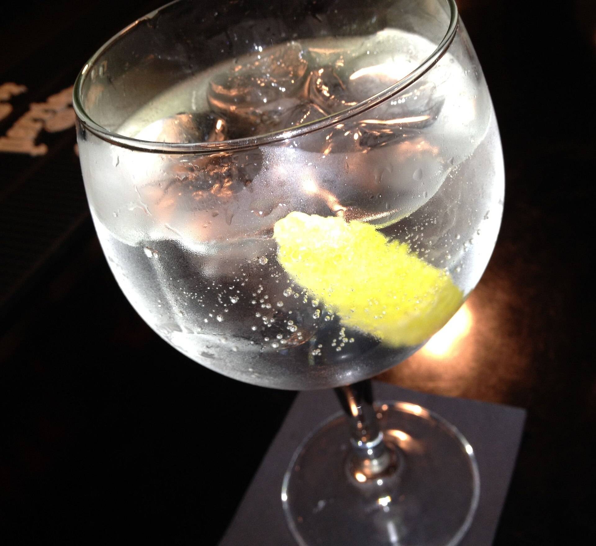 A balloon glass of gin and tonic with lemon, lit warm on a dark table