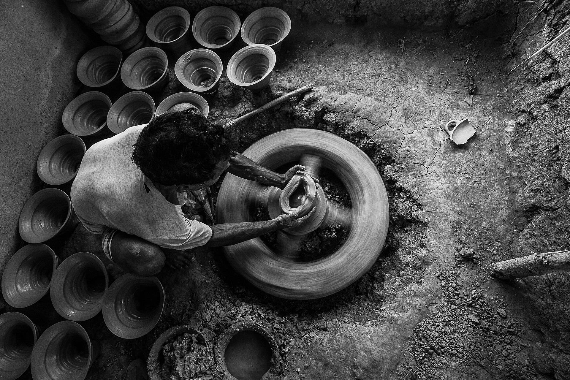 A potter at a kick wheel among drying clay bowls, seen from above