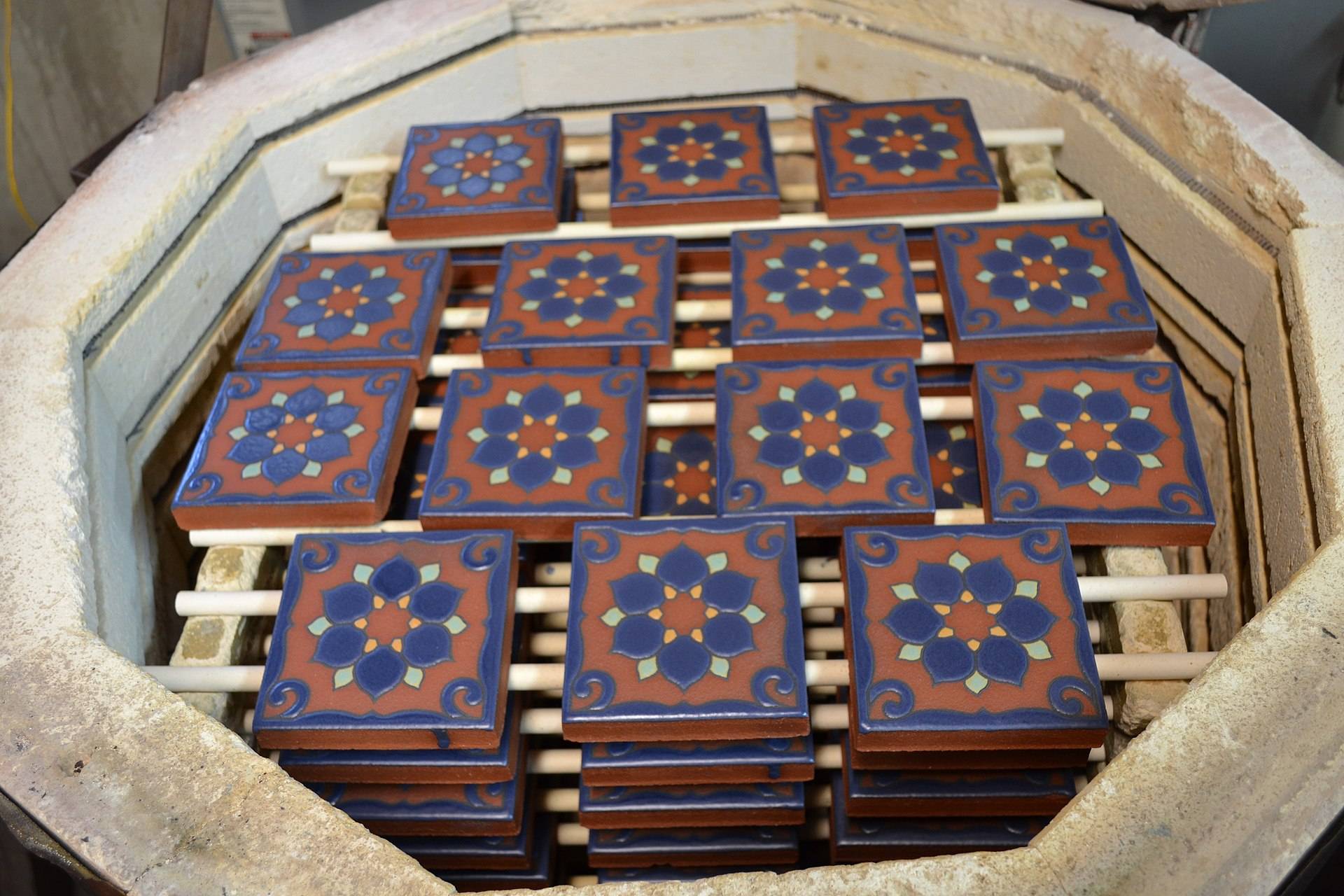 An open kiln stacked with glazed blue and terracotta tiles on refractory shelves