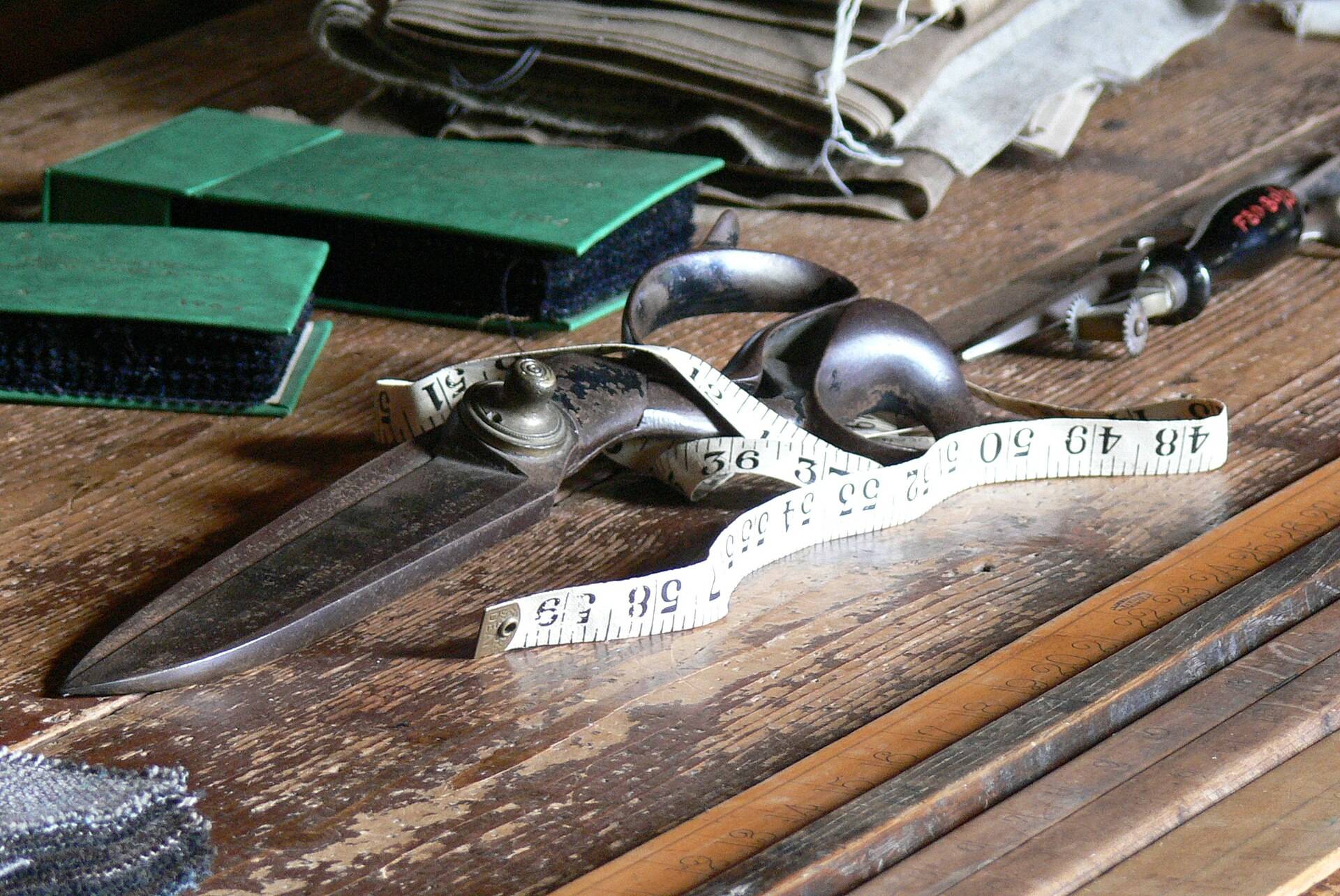 Tailor's shears, a tape measure and a folded length of cloth on a worn wooden table