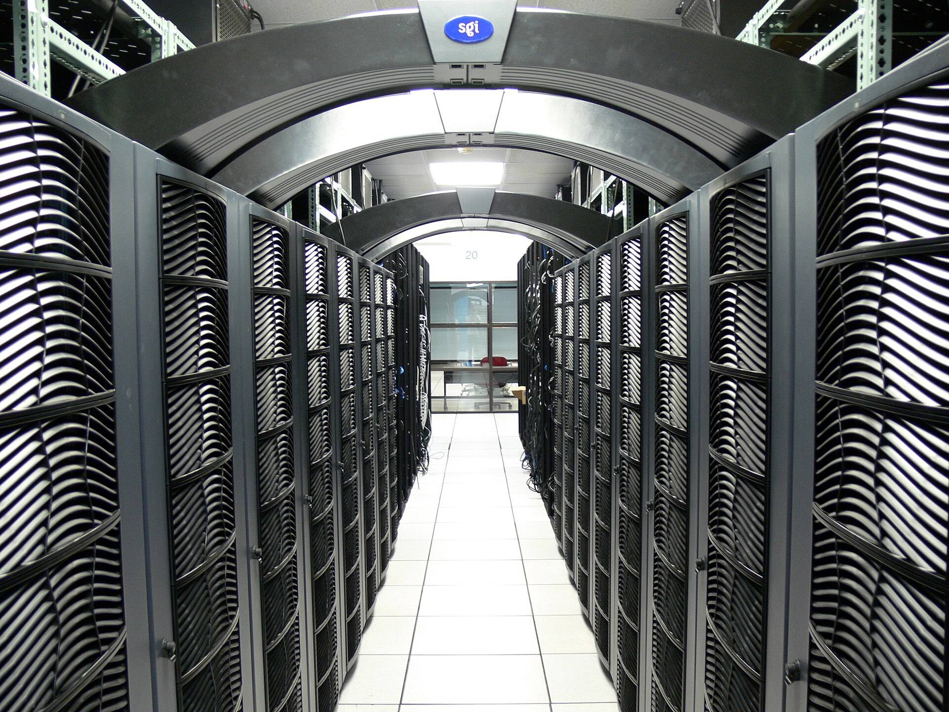A long aisle between black server racks under a white ceiling in a data centre