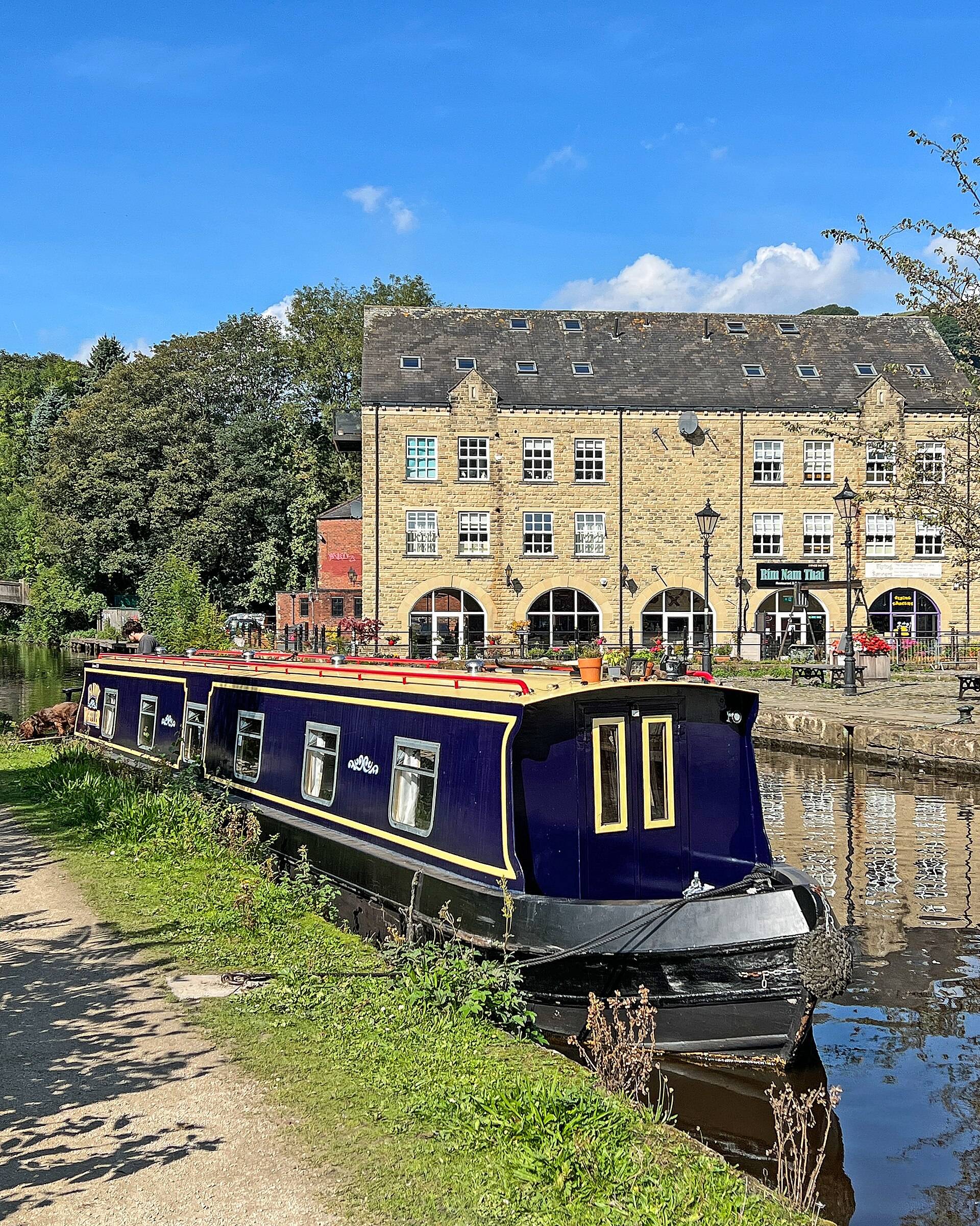 A narrowboat moored on the canal below a tall stone mill