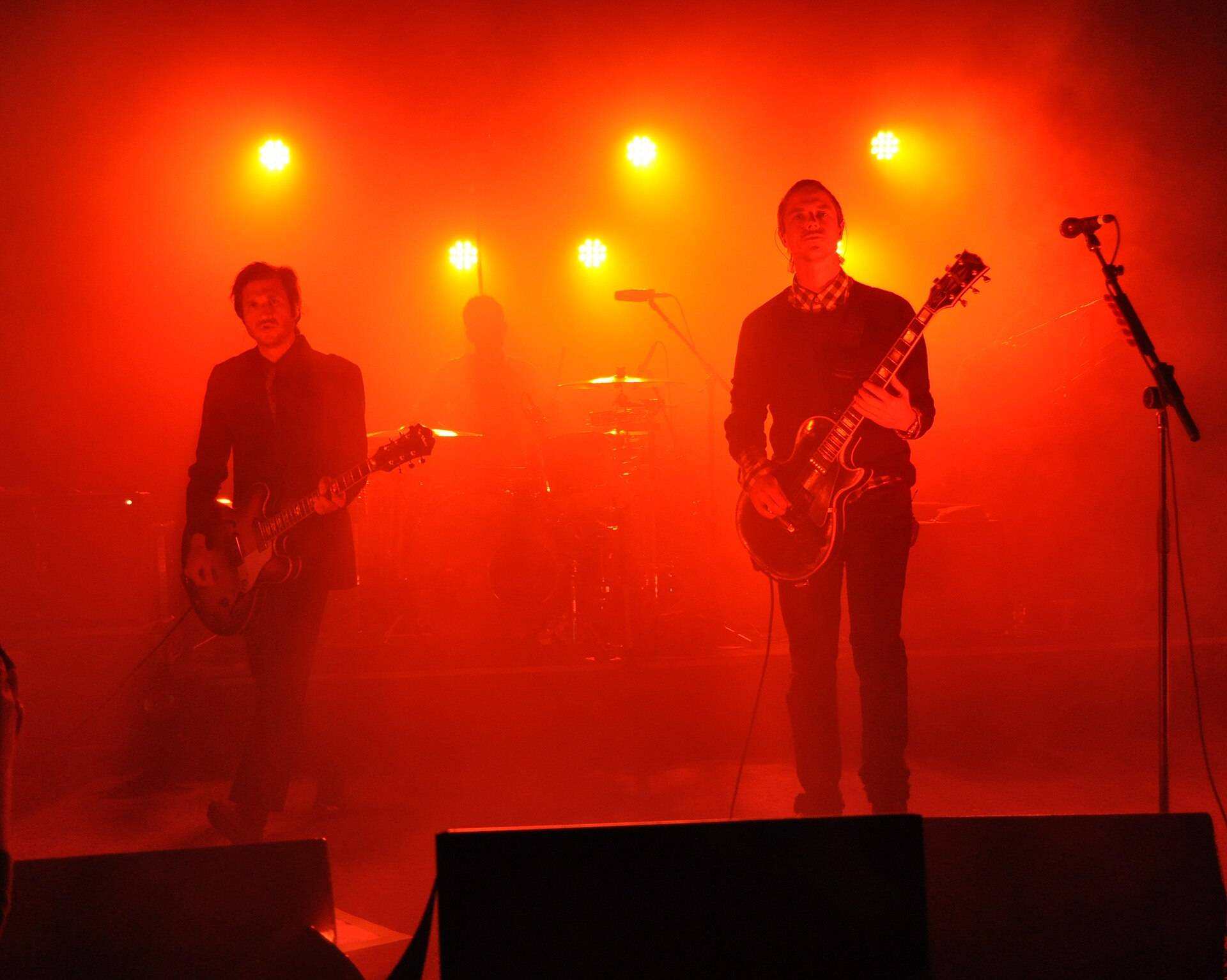 Two guitarists in silhouette on a small stage, lit through smoke