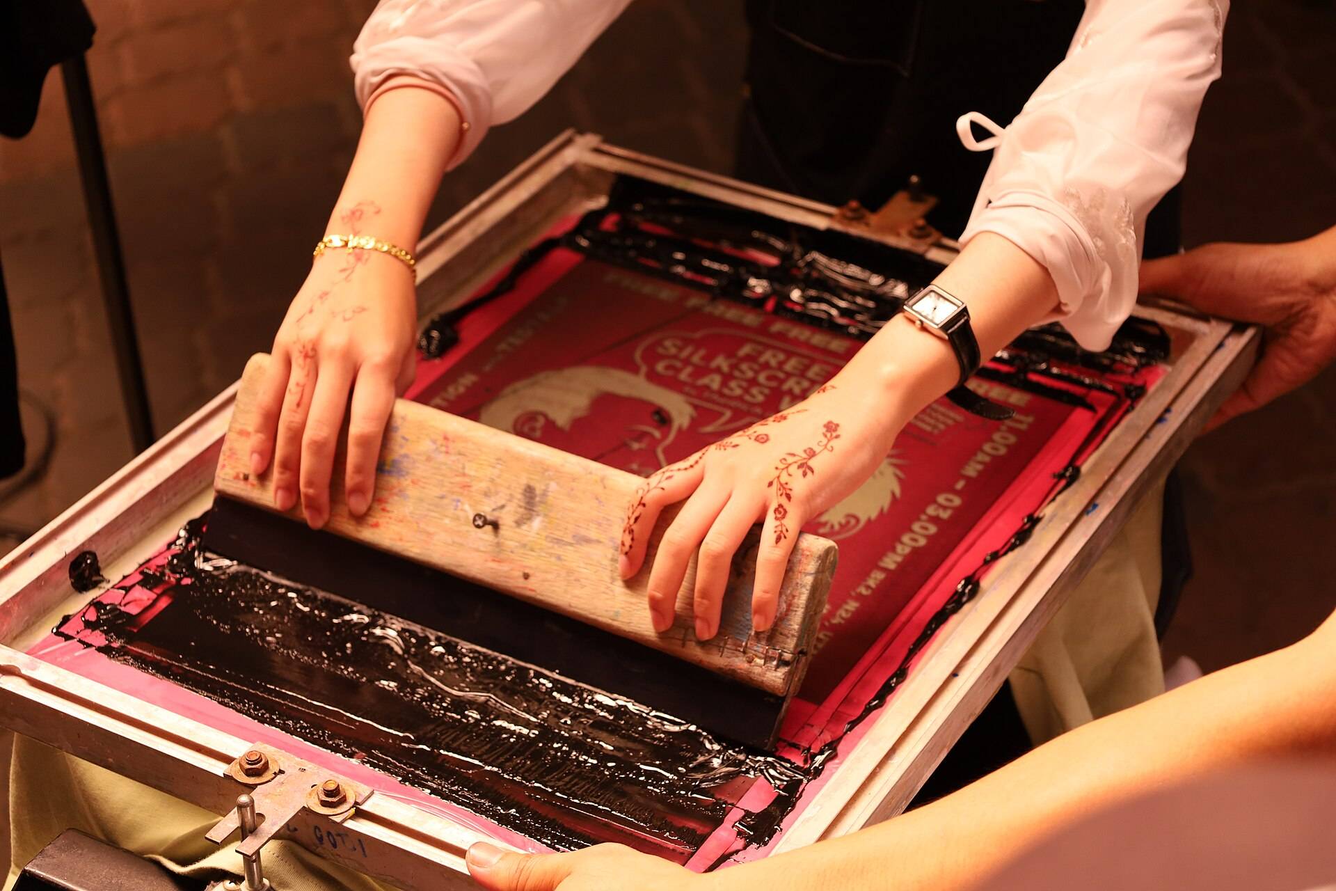 Two hands pulling a squeegee across a silkscreen frame