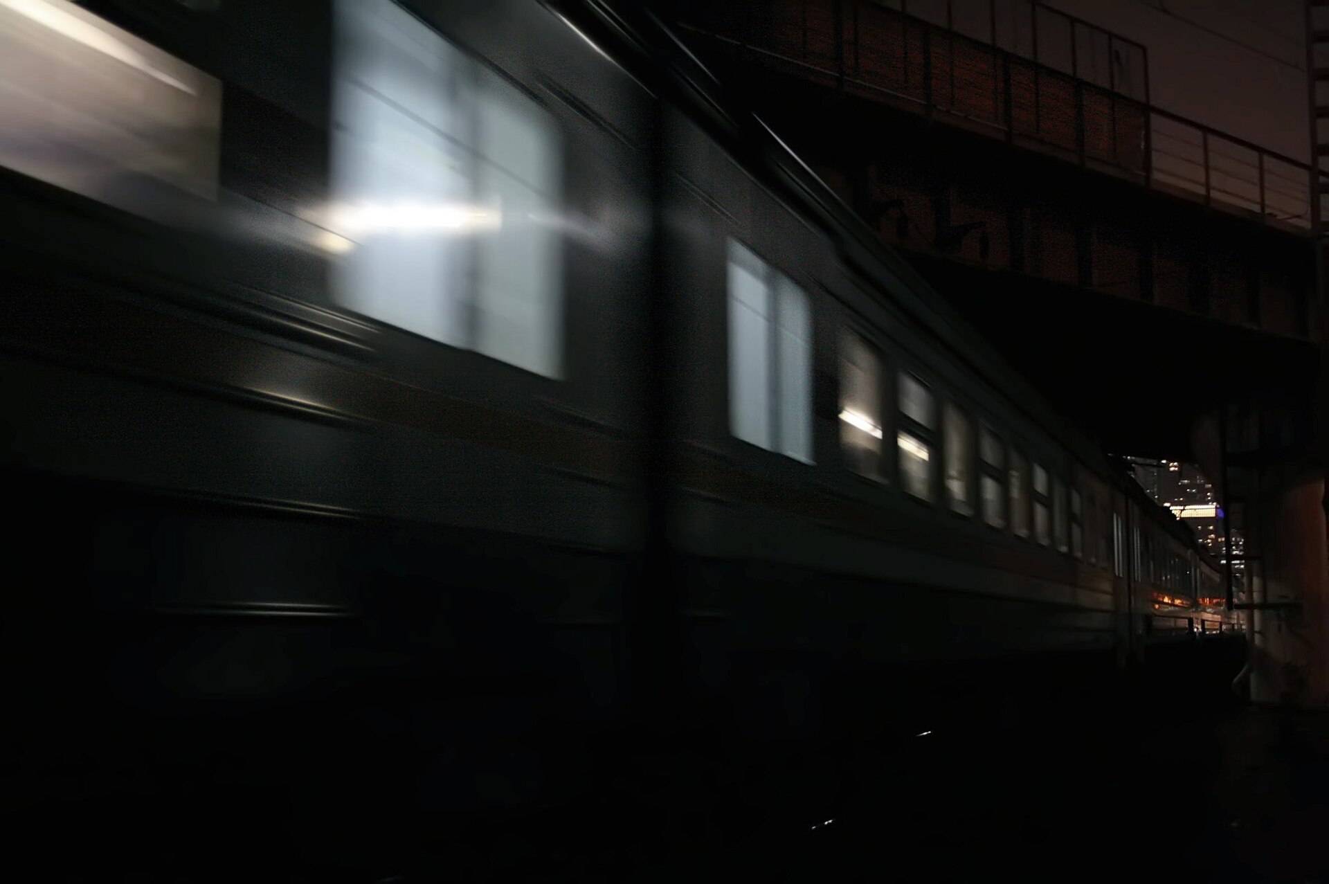 A dark train sliding past at night, its lit windows drawn out in a blur