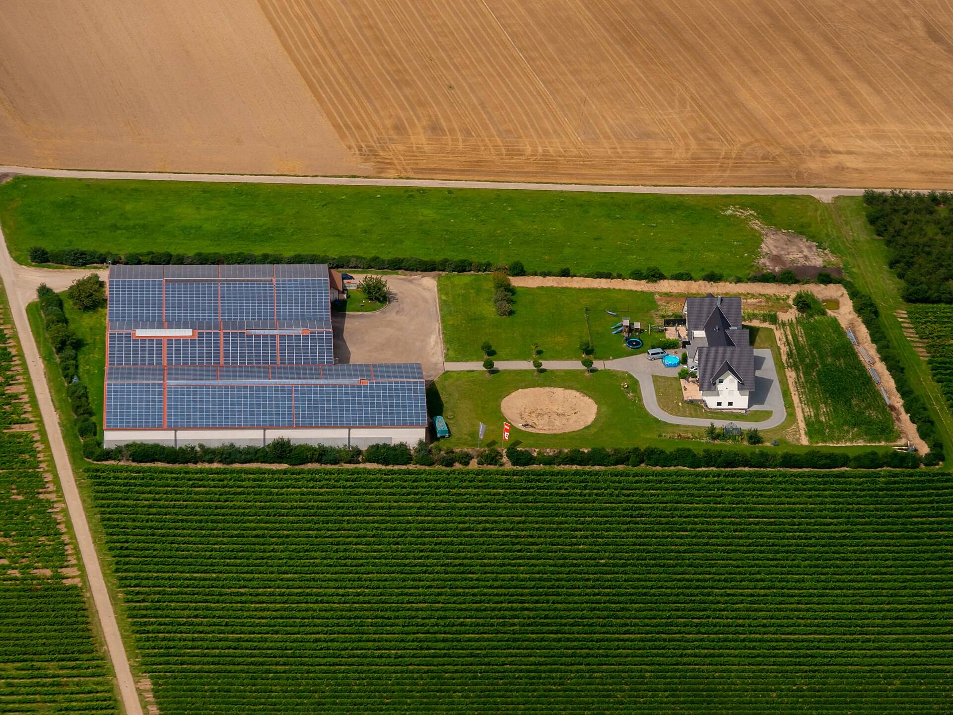 A farmstead with solar panels on its barn roofs between fields, from above