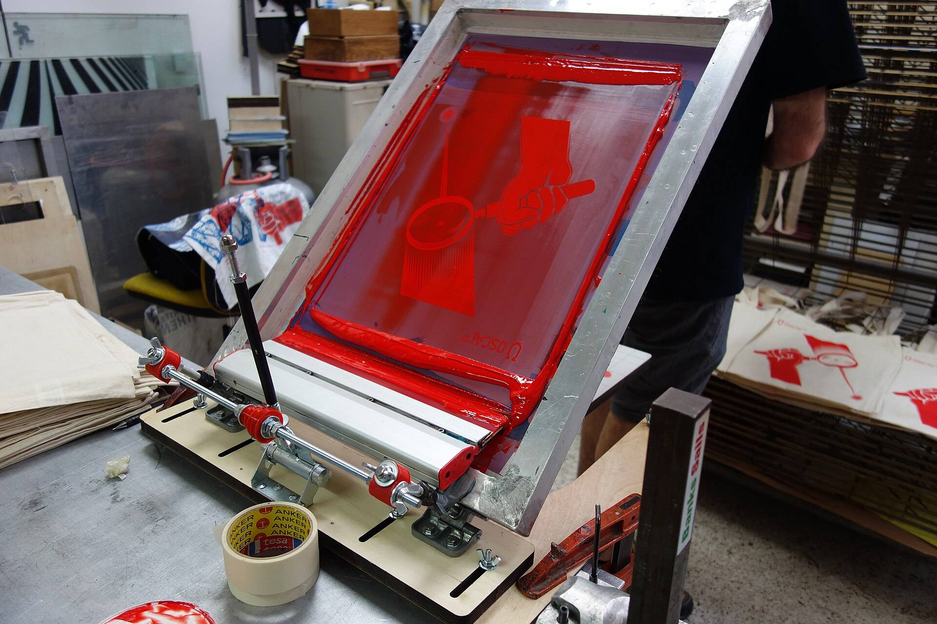 A print frame lifted on its hinged press, a fresh sheet beneath it