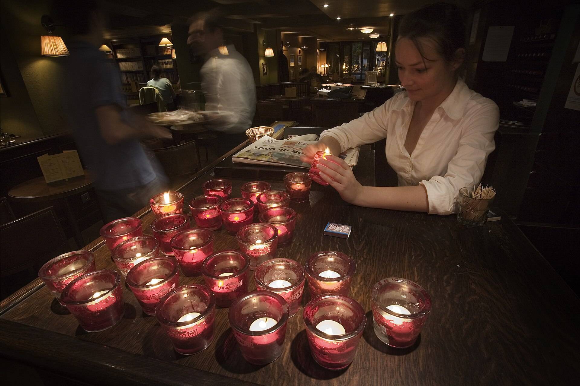 Candles in red glass lit along a dark bar counter