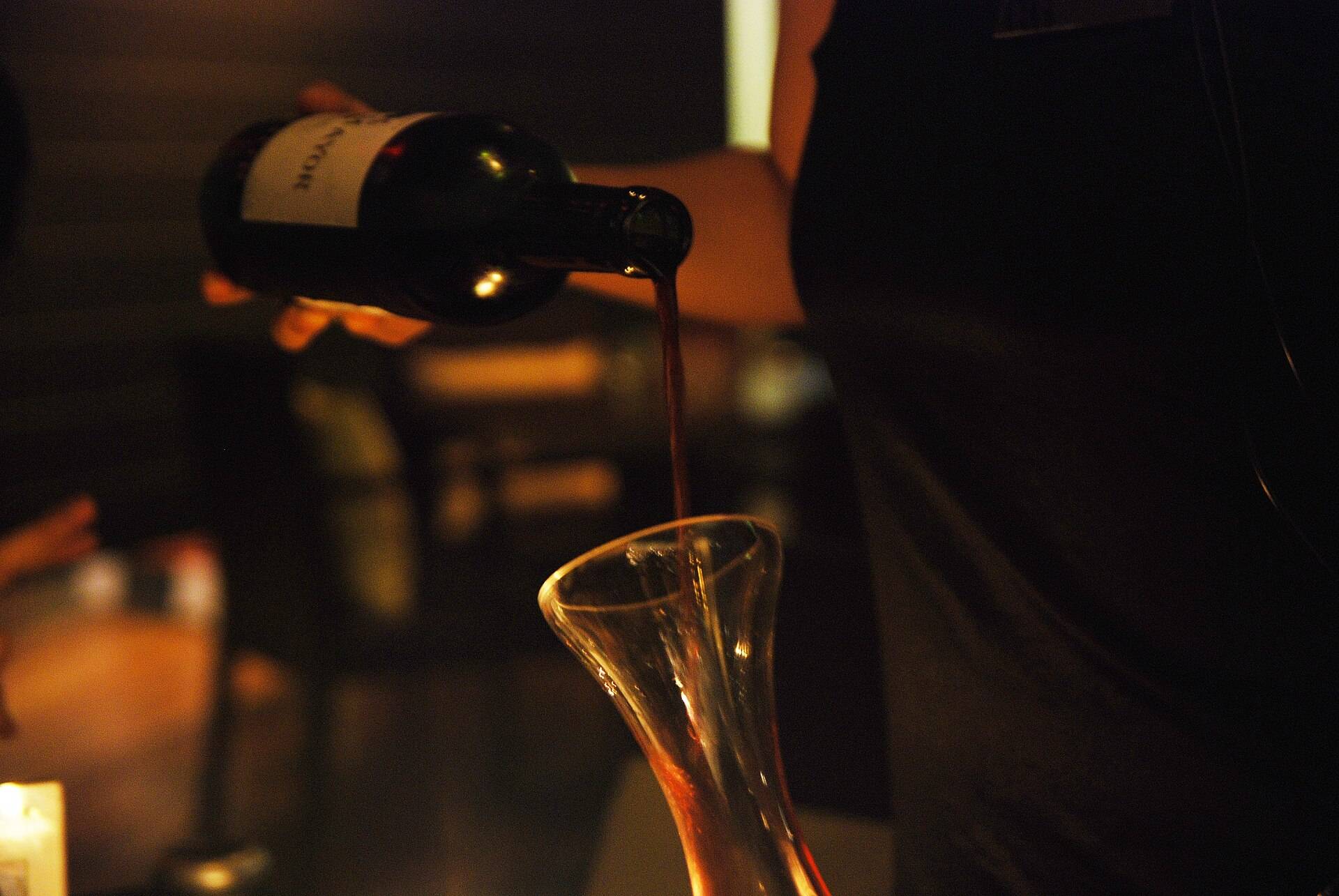 Wine poured from a bottle into a glass decanter in low light