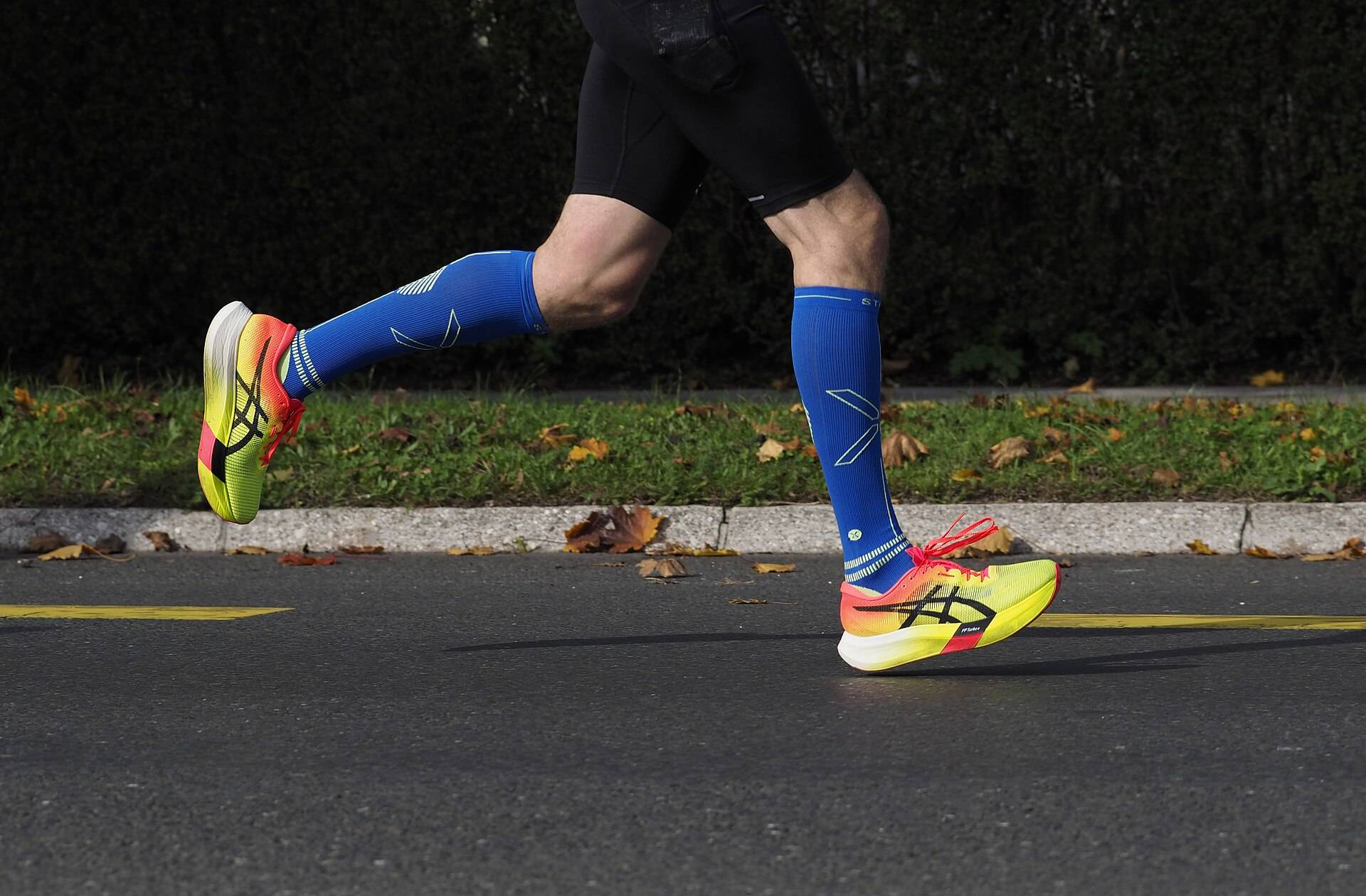 A runner's legs in compression socks and racing shoes, mid stride on the road