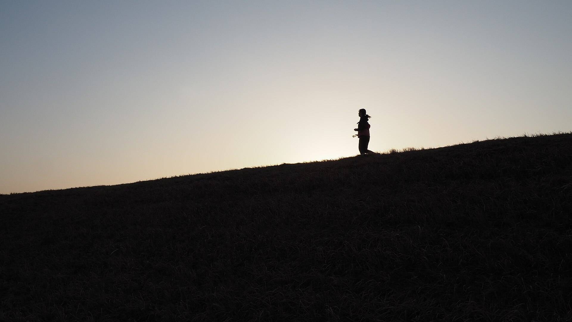 A lone runner silhouetted on a hill crest against a pale sky