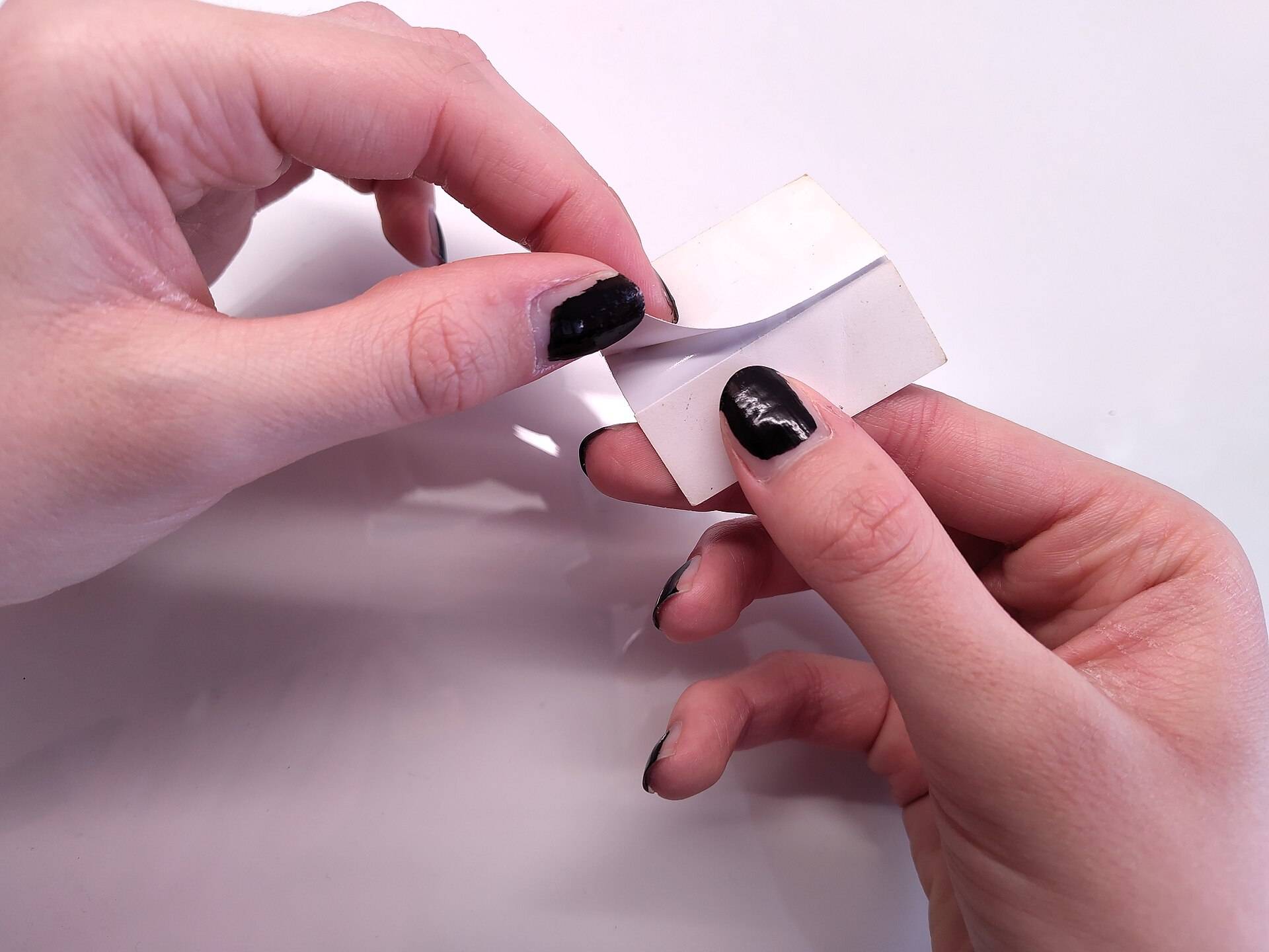Two hands peeling the backing off a white die-cut sticker