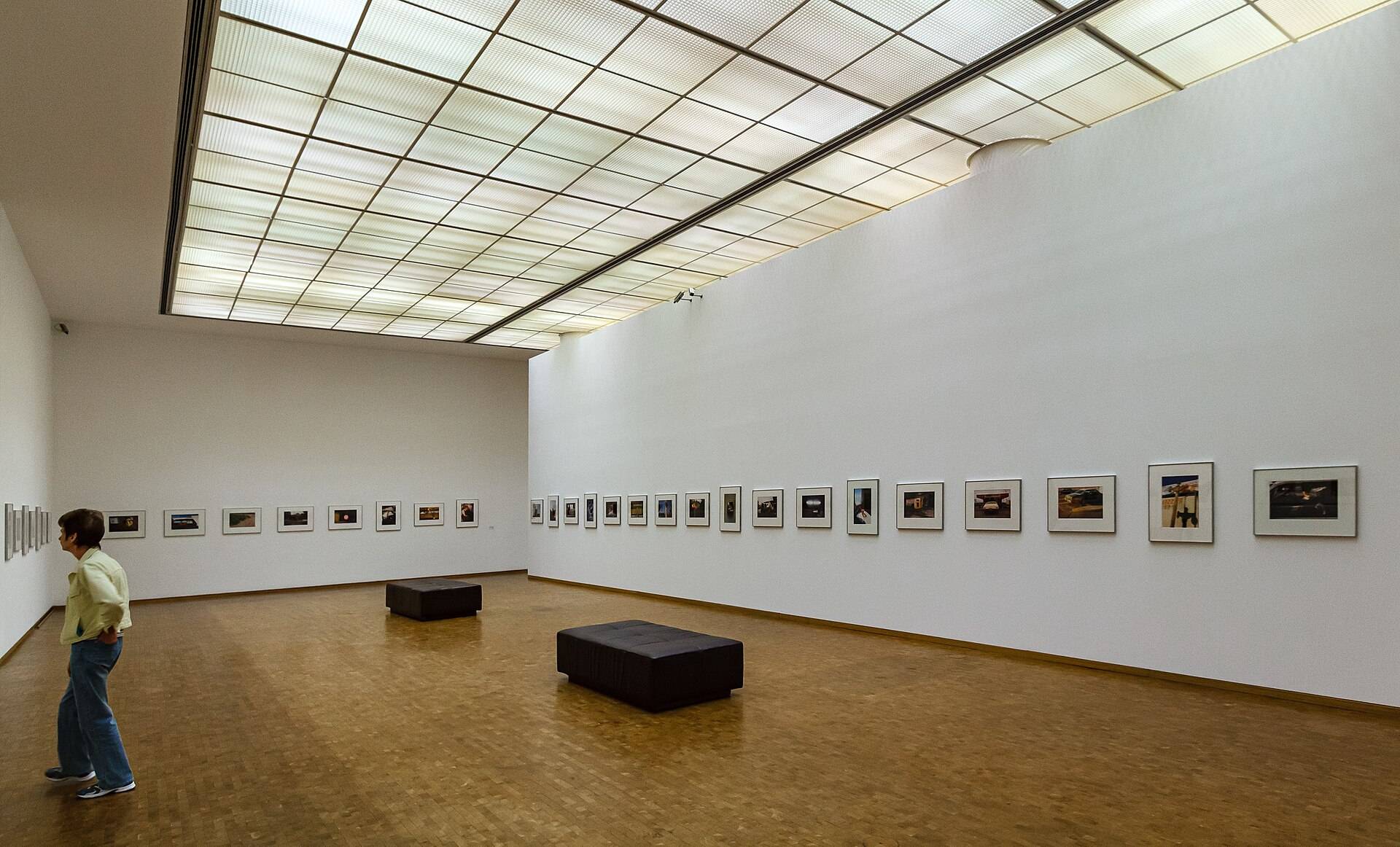 A long white gallery hung with framed photographs, one visitor looking along the wall