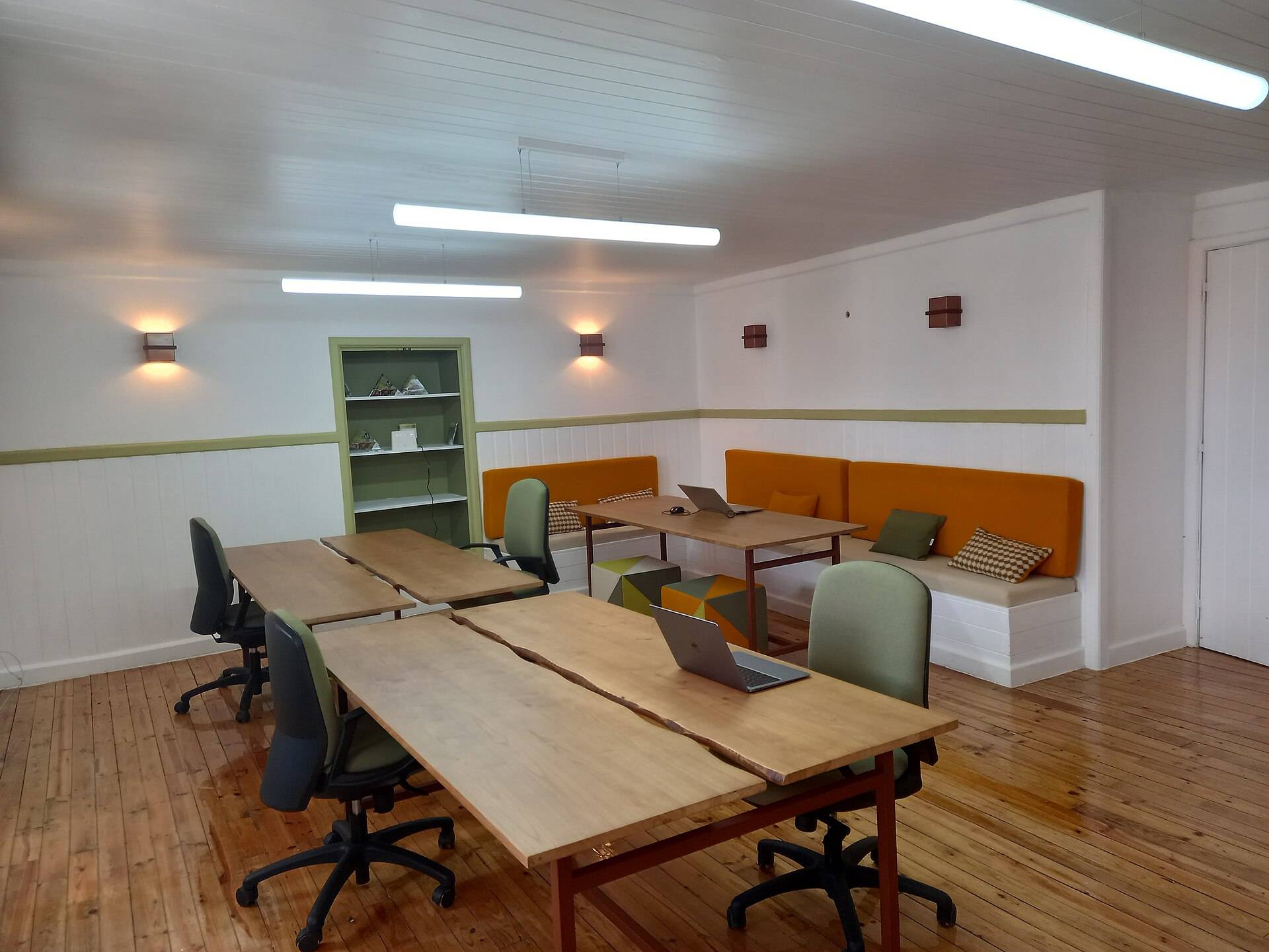 A white-panelled workroom with long timber tables, green chairs and an orange window bench