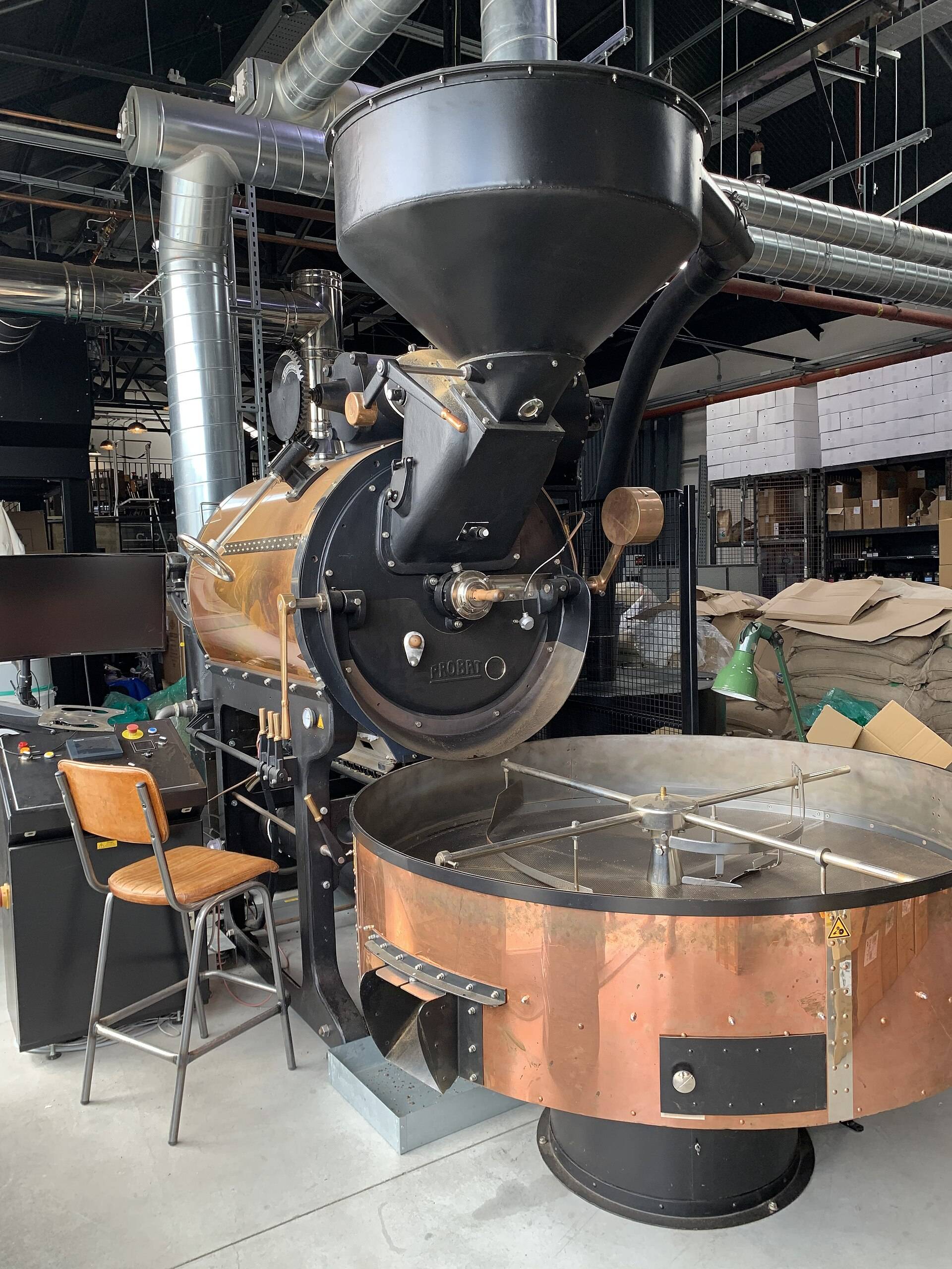 A drum coffee roaster above its copper cooling tray