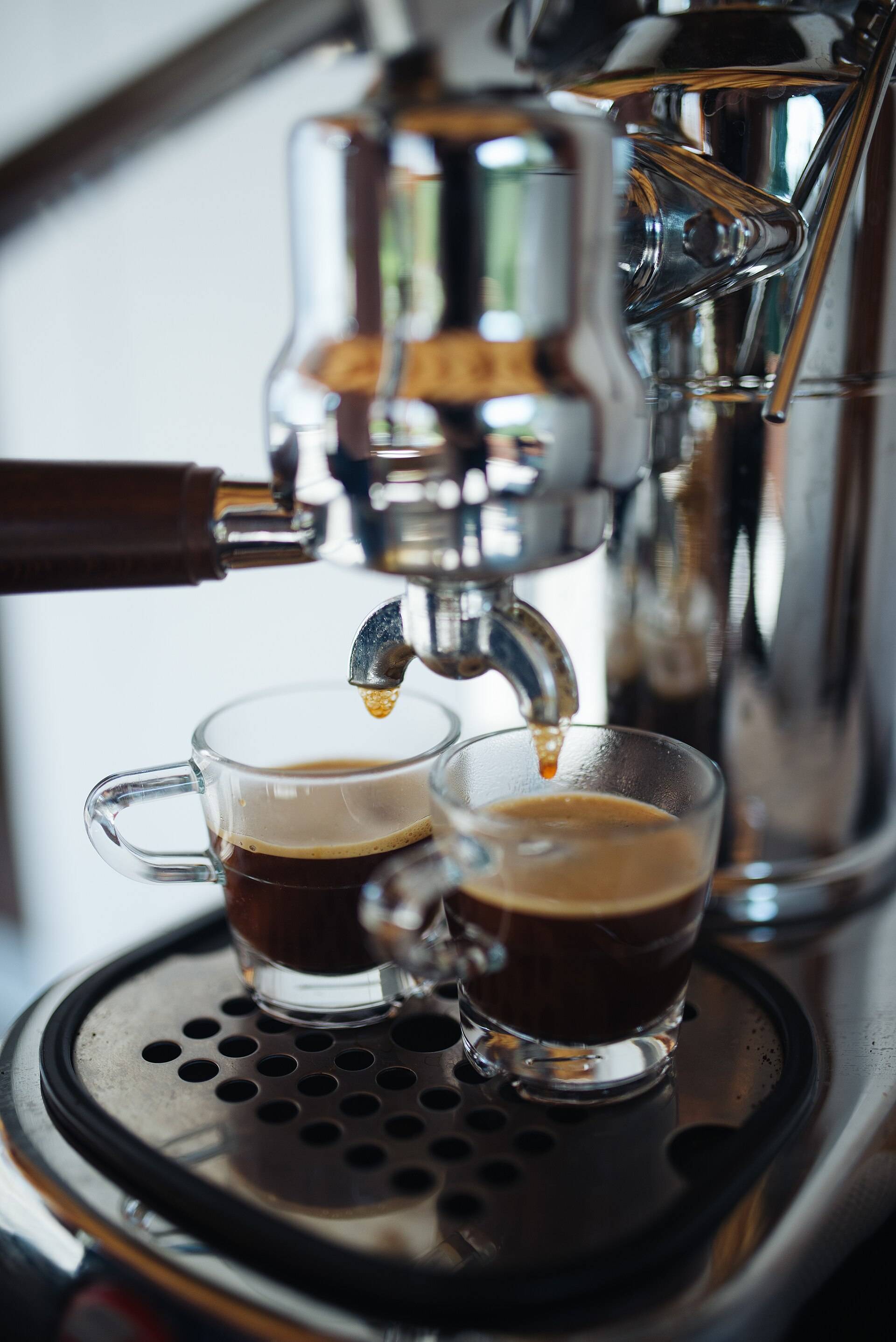 Espresso streaming from a chrome machine into two glass cups