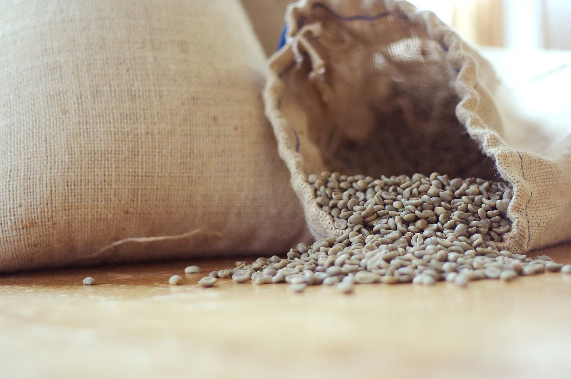 A burlap sack spilling green coffee beans across a wooden table