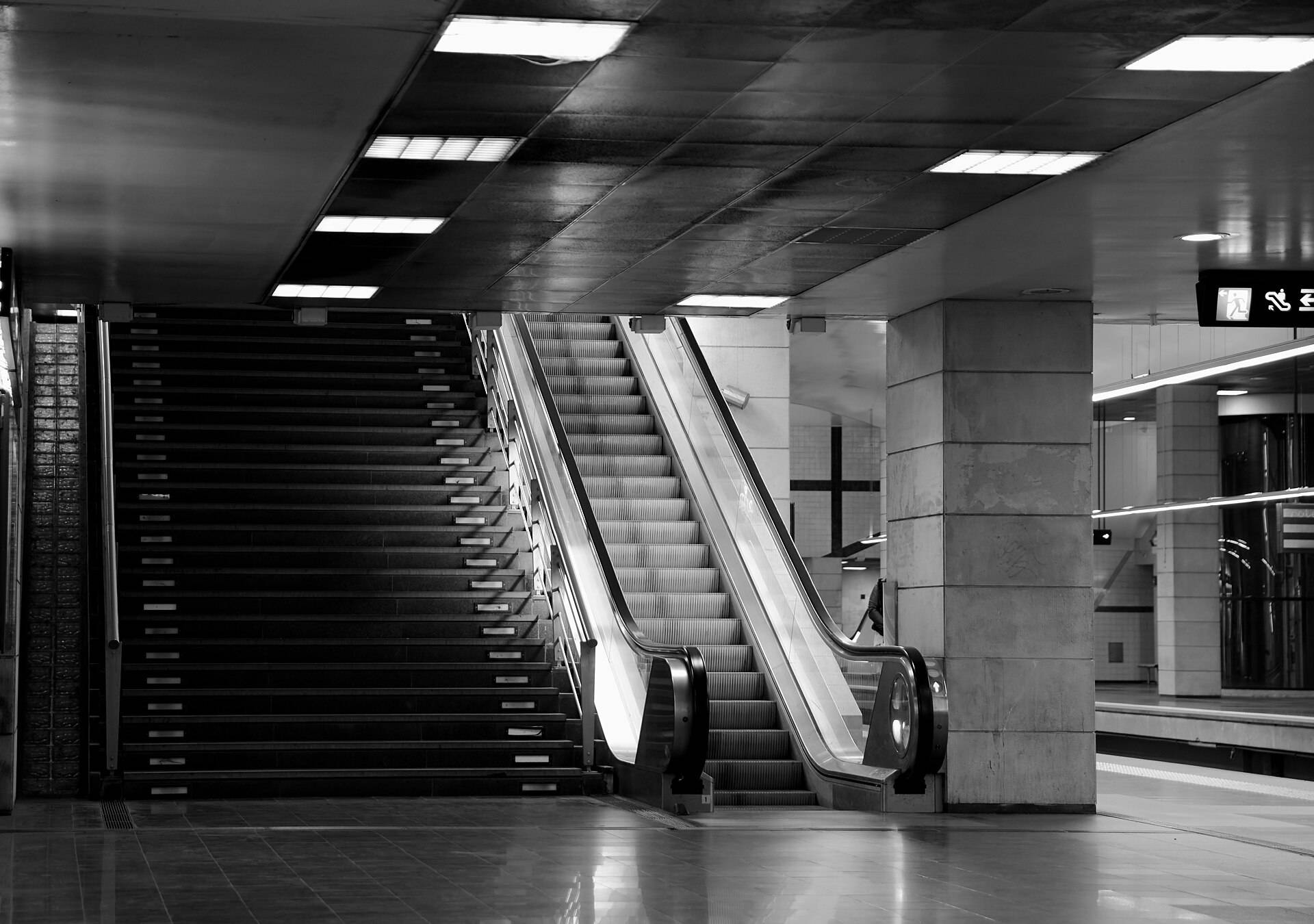 A wide stair and an escalator rising beside a square pillar inside a Lisbon metro station
