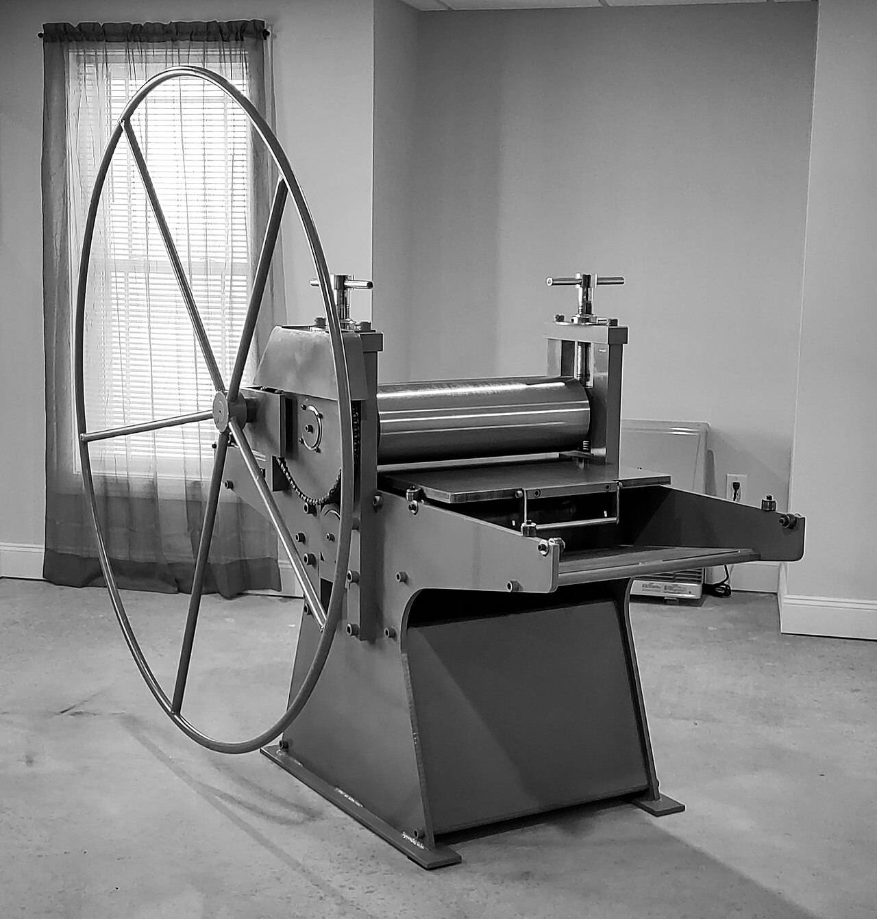 A spoked etching press standing in a bare print room