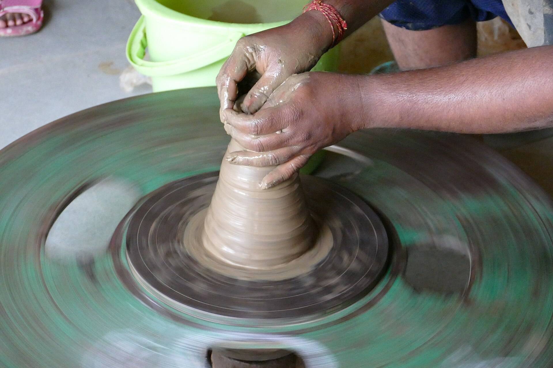 A potter's hands closing a clay cone on a fast spinning wheel