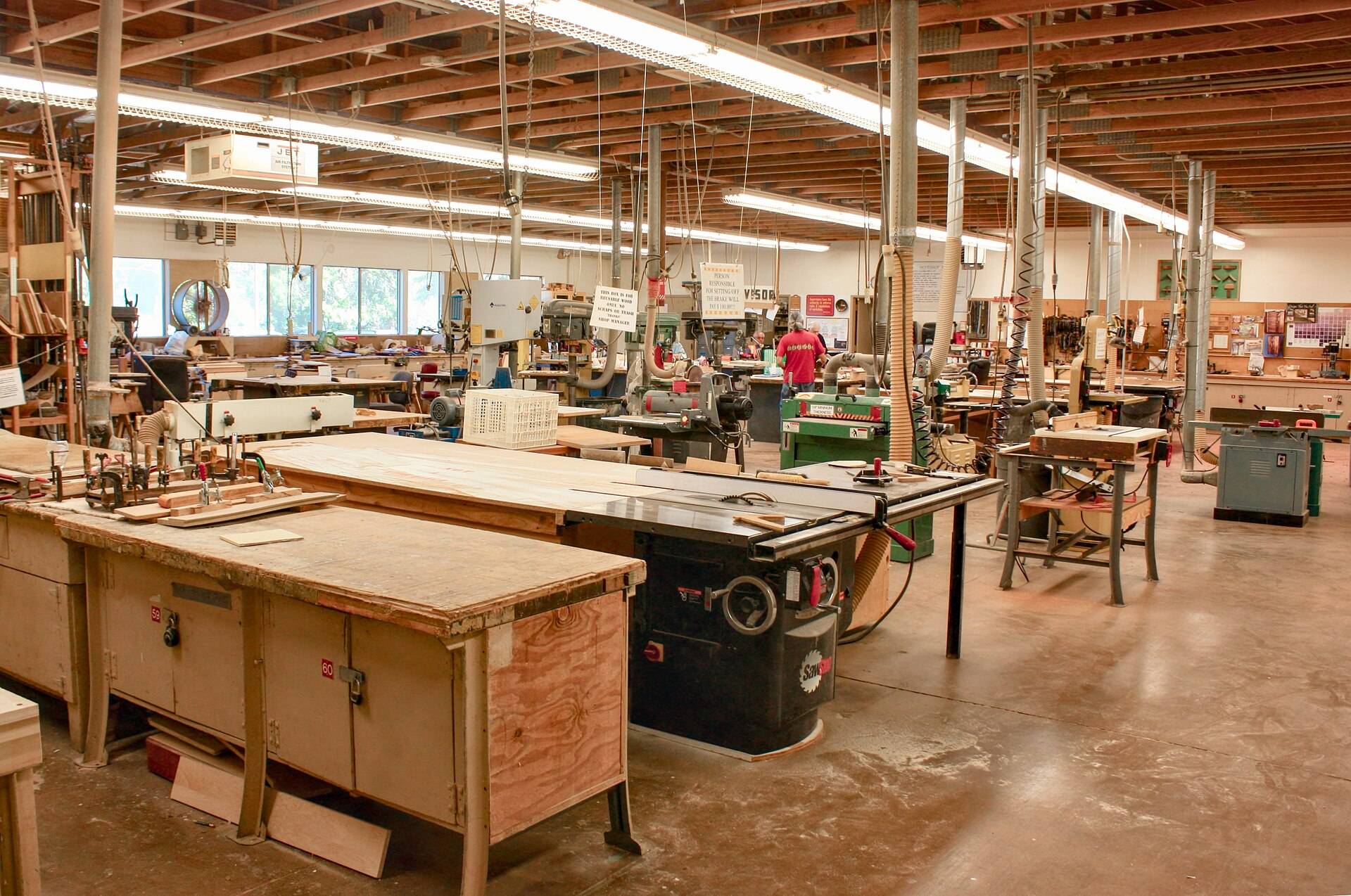 A long daylit woodshop of workbenches and machines