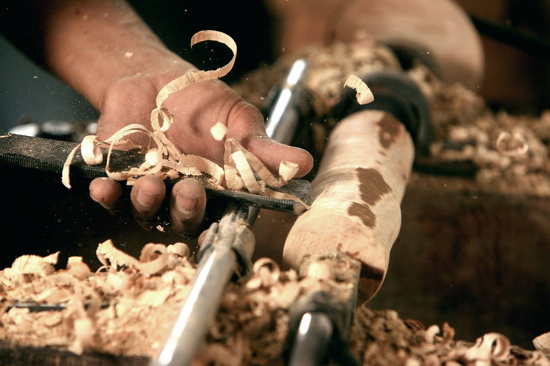 Hands steadying a gouge against a lathe as the shavings fly